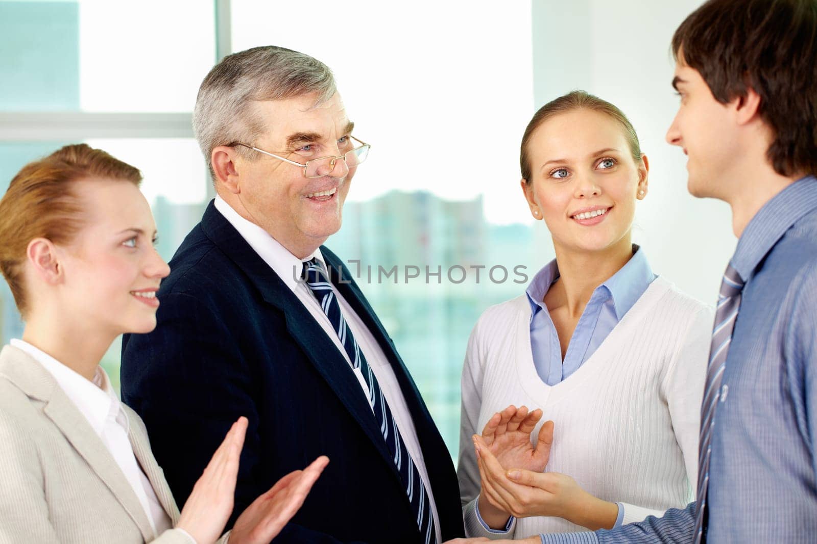 Photo of successful businessmen handshaking after striking deal with applauding women near by