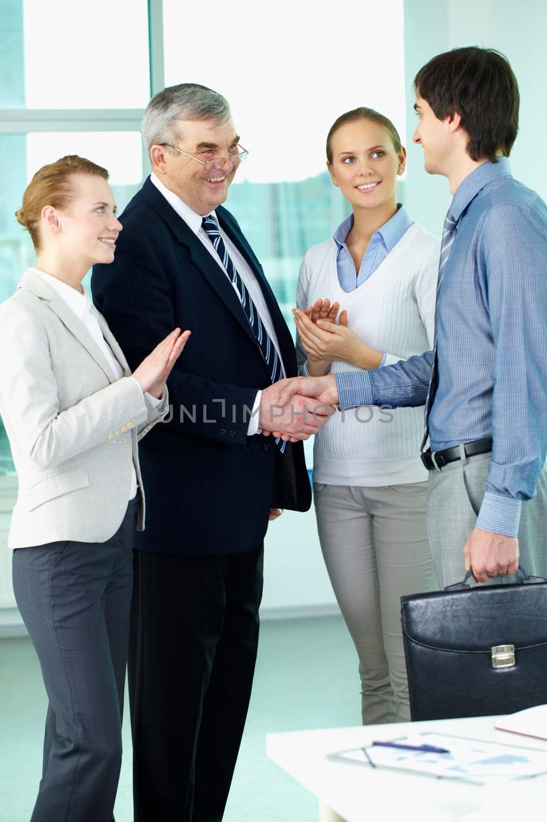 Photo of successful businessmen handshaking after striking deal with applauding women near by