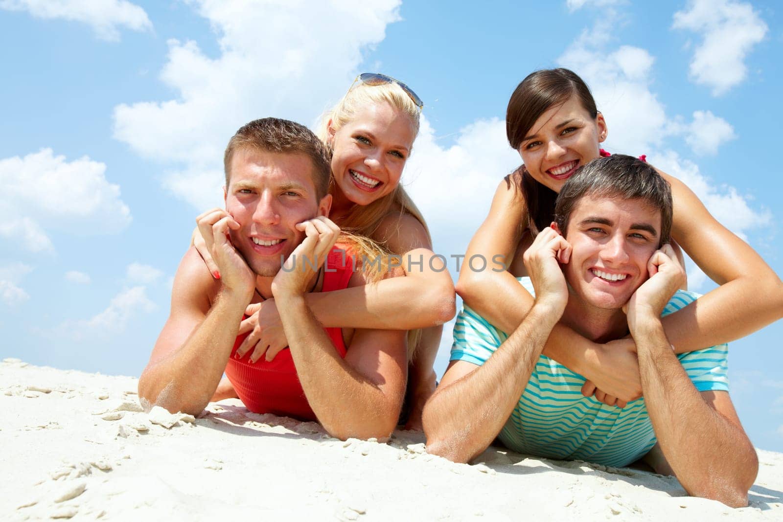Two happy couples lying on sand and looking at camera