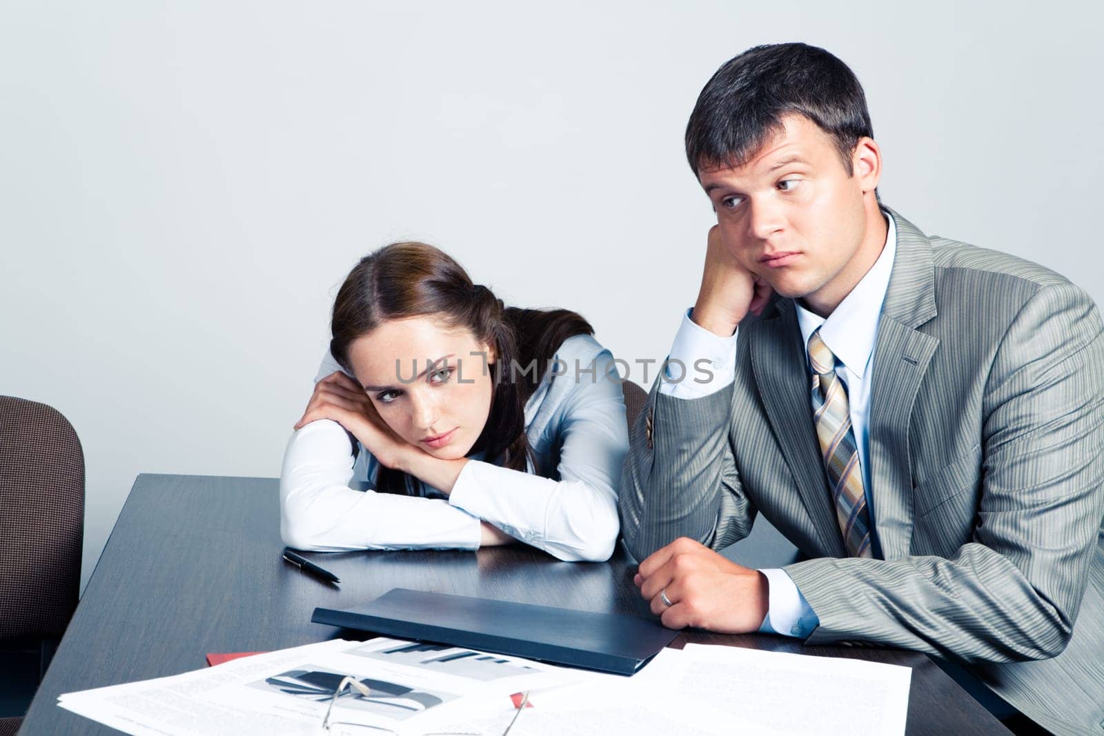 Portrait of pensive businesswoman and businessman sitting at the table with documents on it