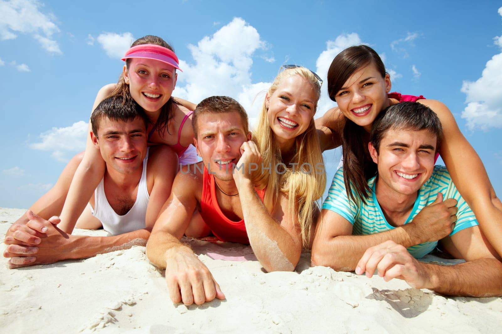 Three happy couples lying on sand and looking at camera