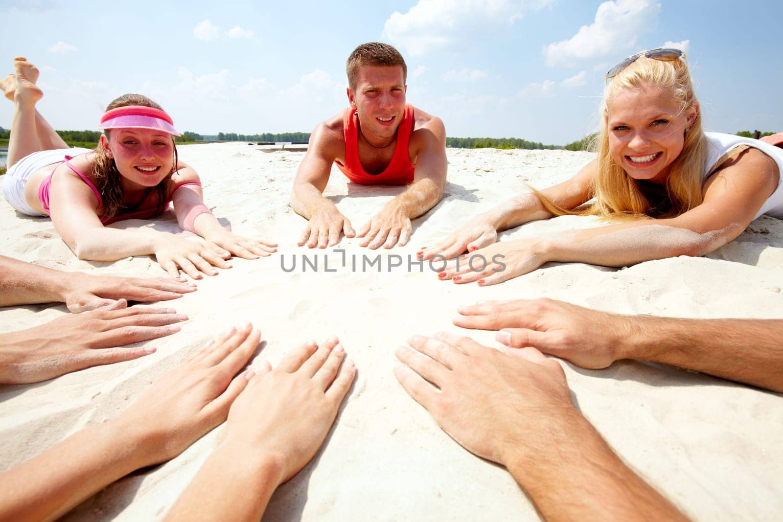 Image of several teens lying on beach and keeping their hands on sand in the form of circle