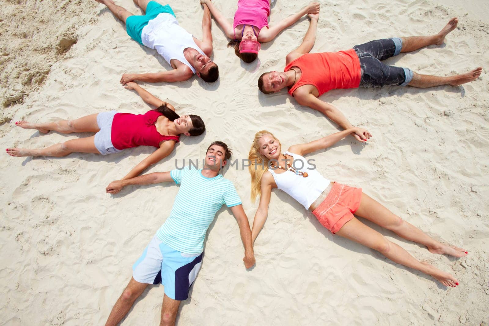 Six friends lying on sand in circle