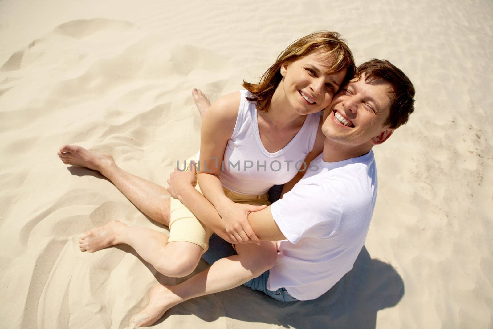 Portrait of amorous couple embracing while sitting on sand