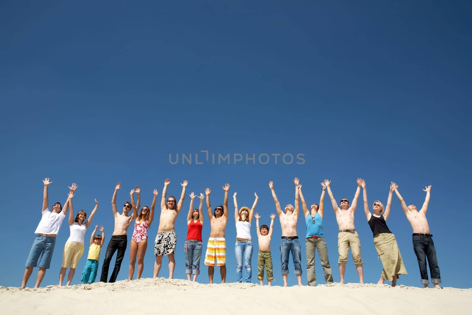 Image of many friends standing on sandy beach with their arms raised against blue sky