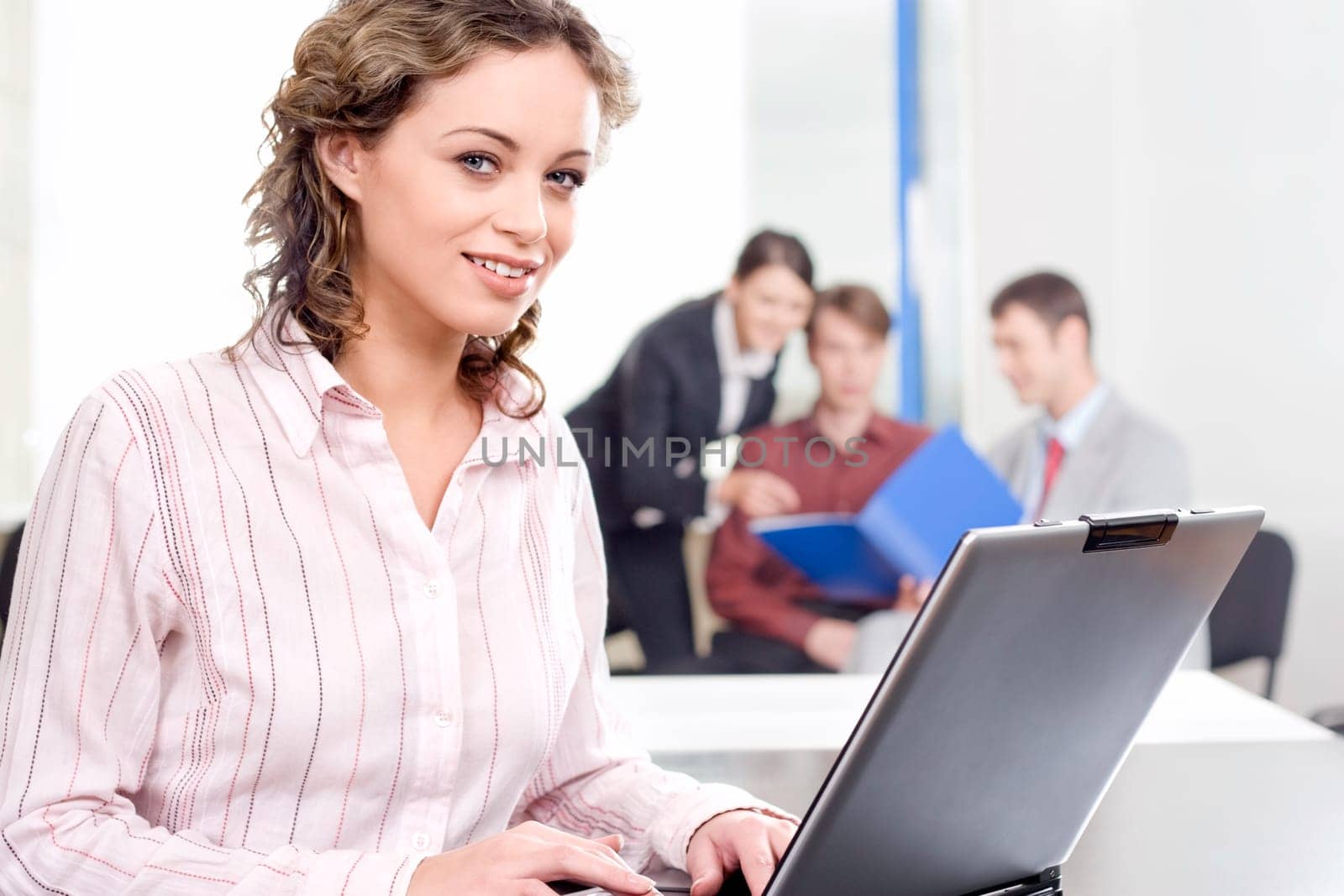 Portrait of beautiful secretary sitting at the table on the background of her co-workers