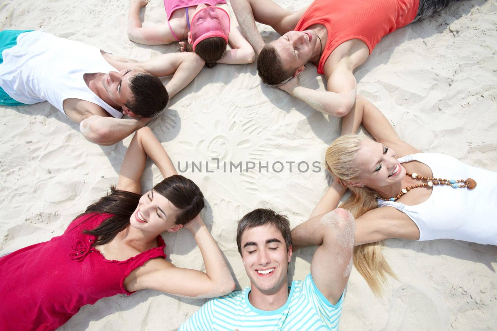 Six friends lying on sand in circle