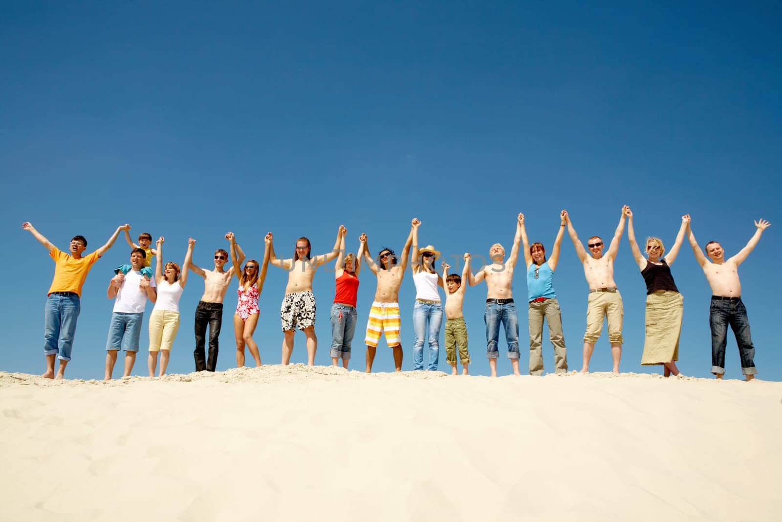 Image of many friends standing on sandy beach with their arms raised against blue sky