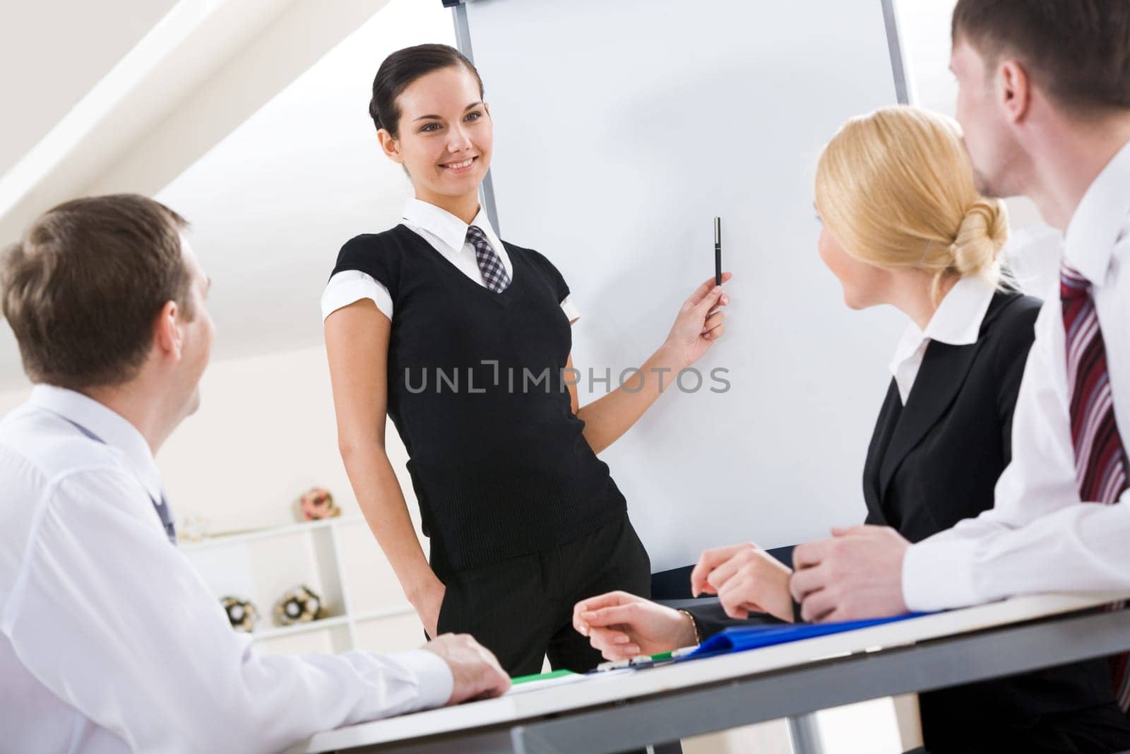 Photo of successful female standing by whiteboard while explaining her idea to colleagues