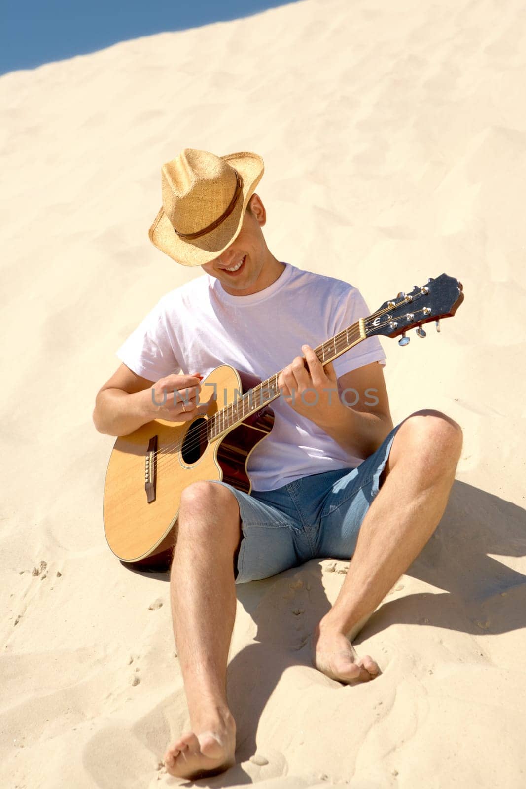 Portrait of happy man in cowboy hat playing the guitar on sandy beach