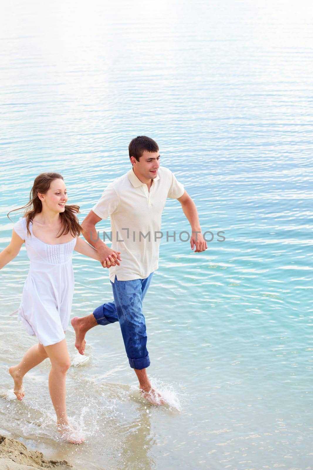 Photo of amorous couple holding by hands while running in water on summer vacation