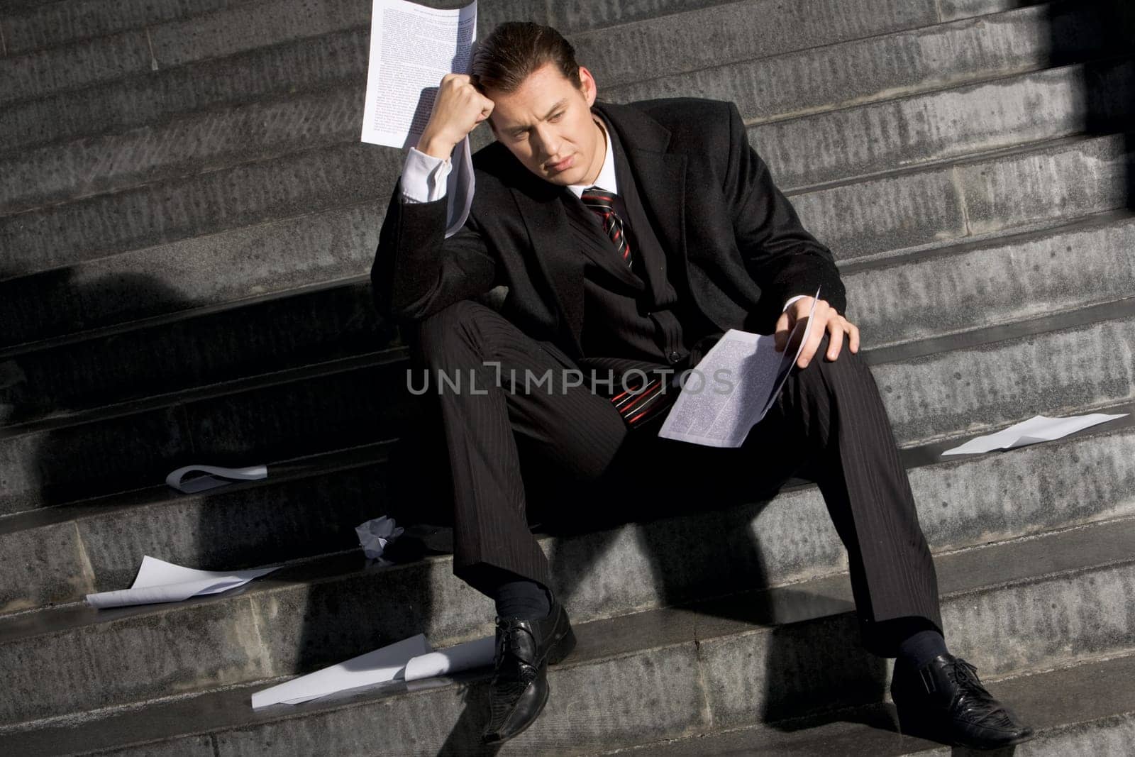Portrait of sad businessman sitting on stairs with papers in hands and lost expression on his face