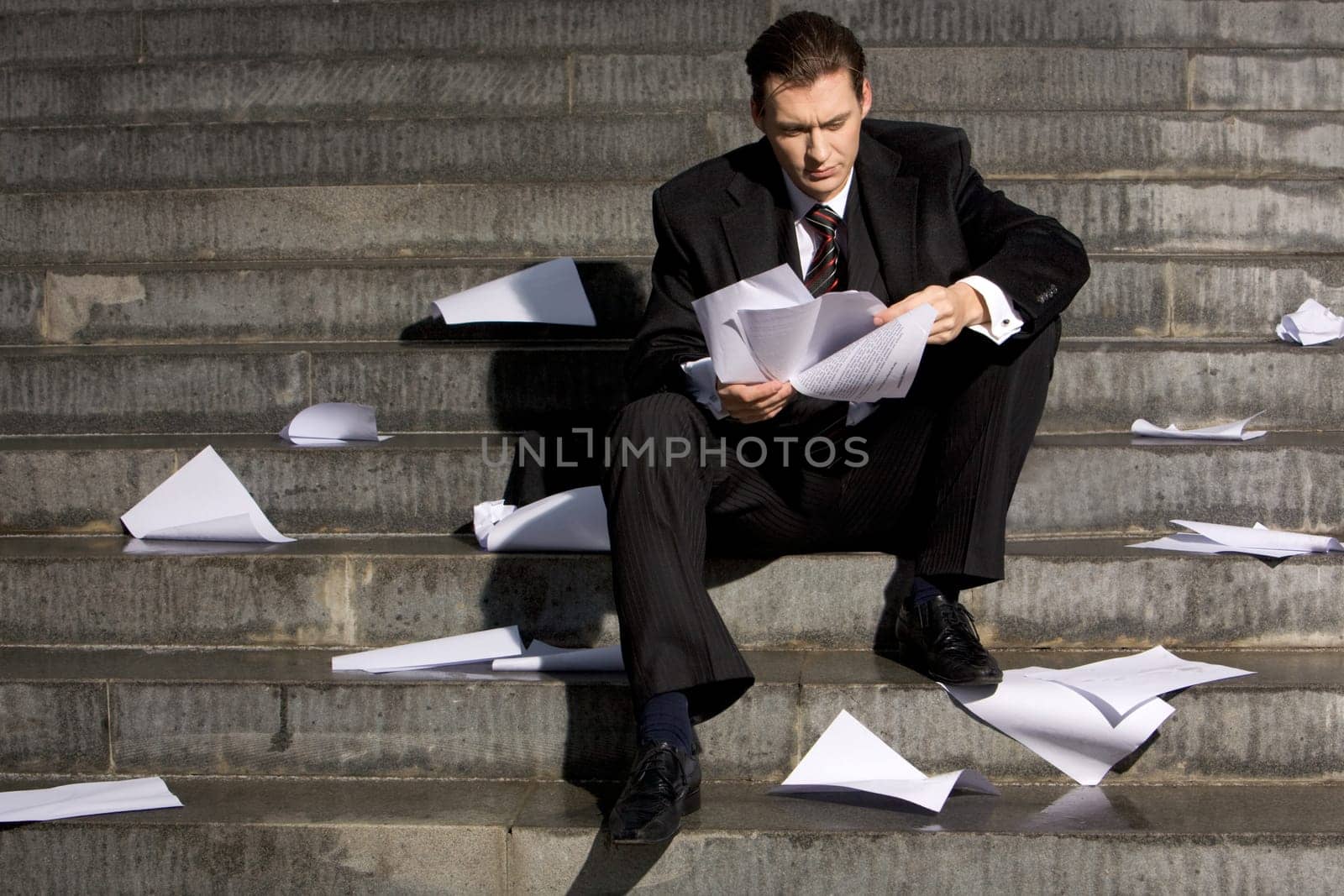 Anxious businessman sitting on stairs while reading documents with pensive expression