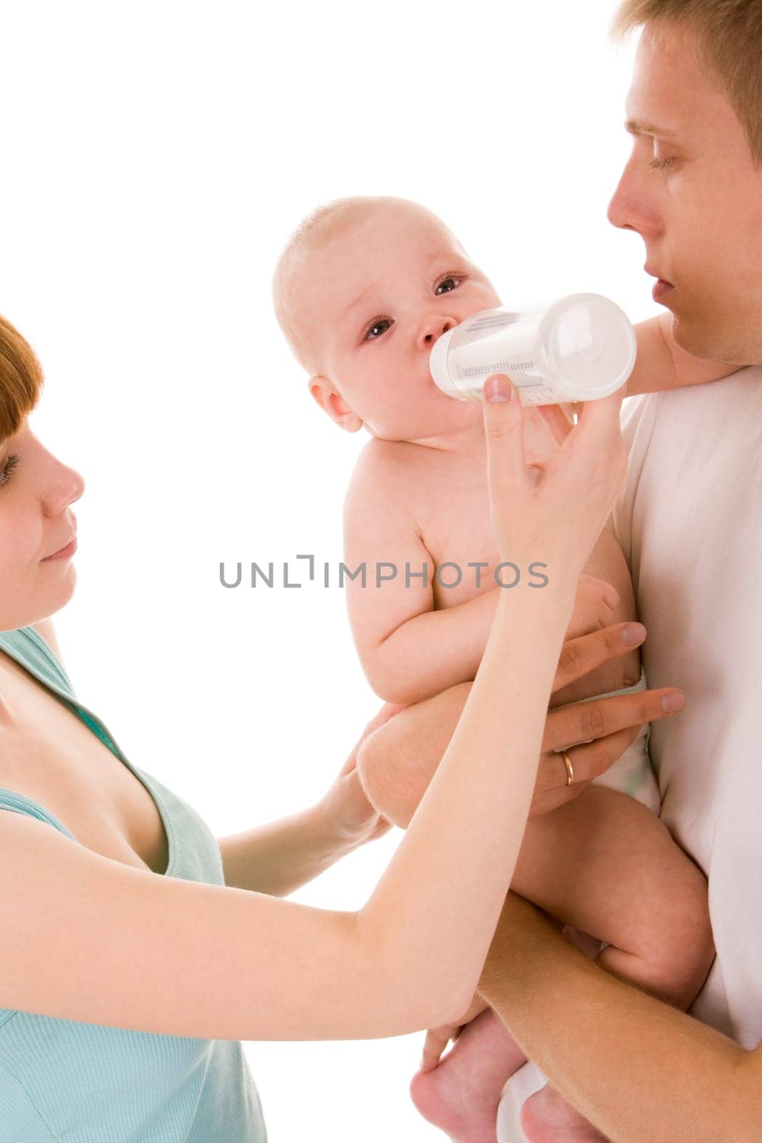 Image of baby drinking milk from bottle in female hand while being held by father