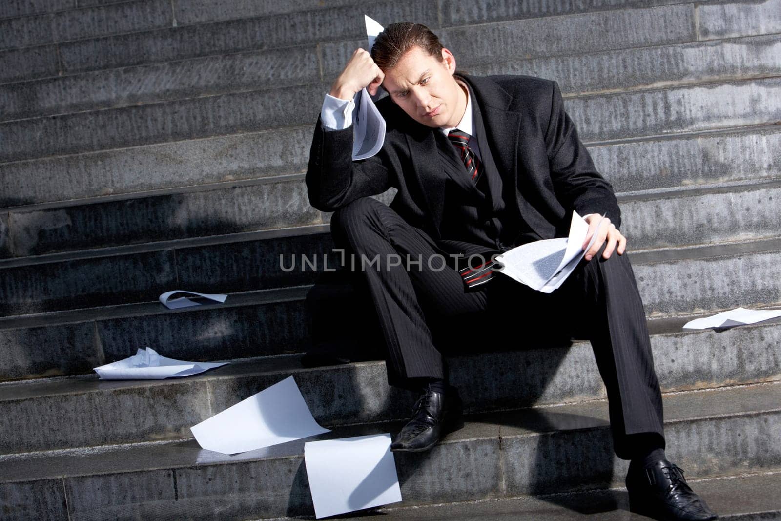 Portrait of sad businessman sitting on stairs with papers in hands and lost expression on his face