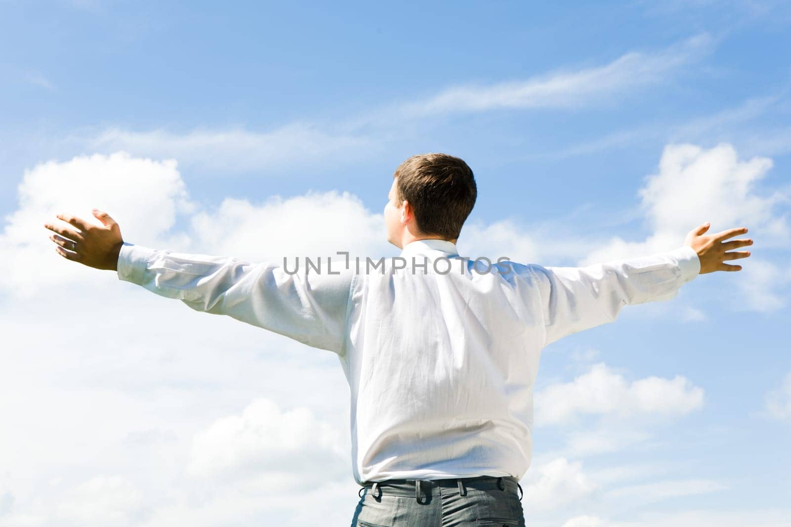 Image of businessman standing aback and looking at blue sky in summer