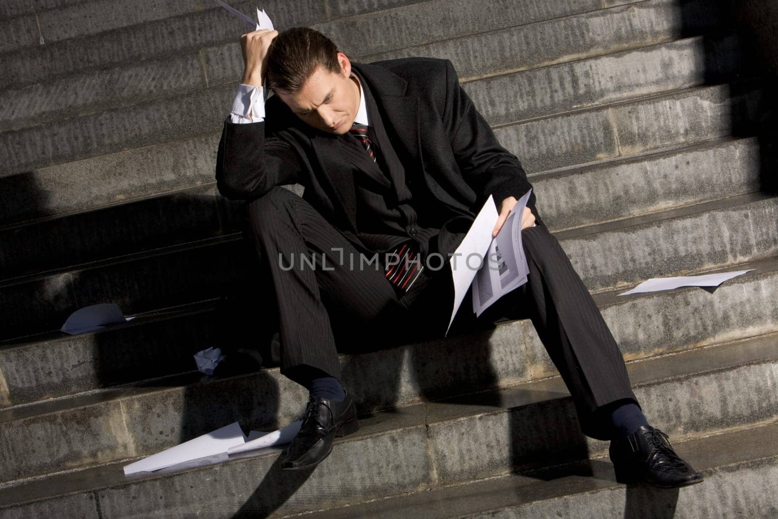 Photo of sad man with papers in hands sitting on stairs with no idea what to do