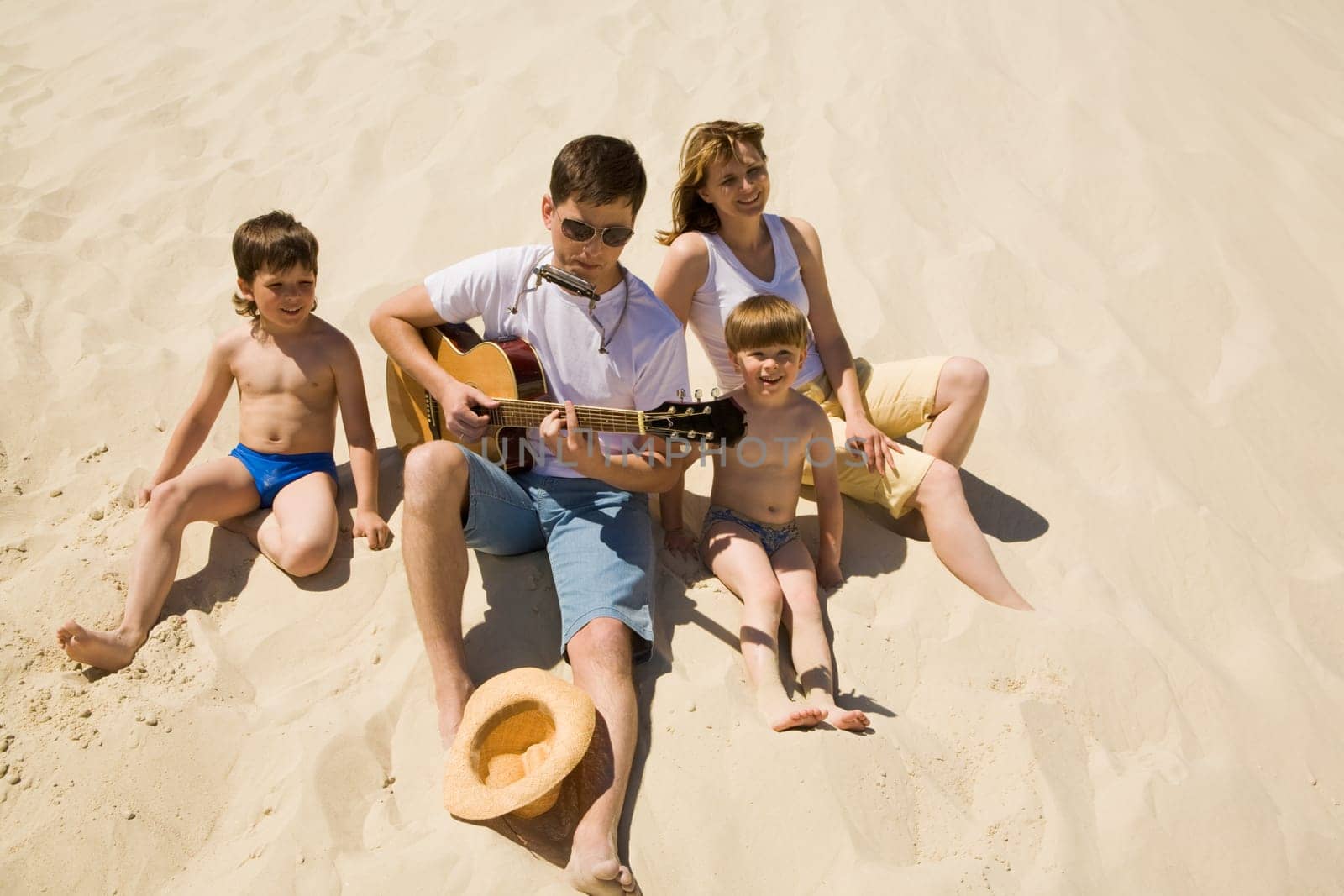 Image of cheerful man playing the guitar with his sons and wife near by