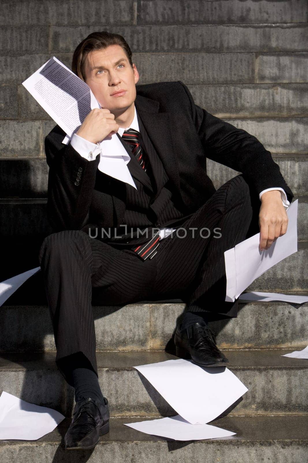 Portrait of depressed manager sitting with papers in hands and around him while looking slightly upwards