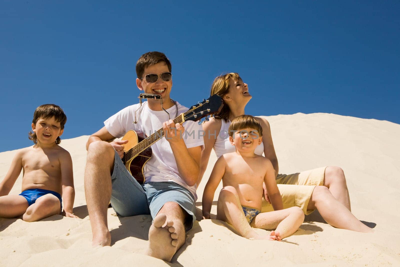 Portrait of cheerful man playing the guitar with his sons and wife near by and enjoying the music