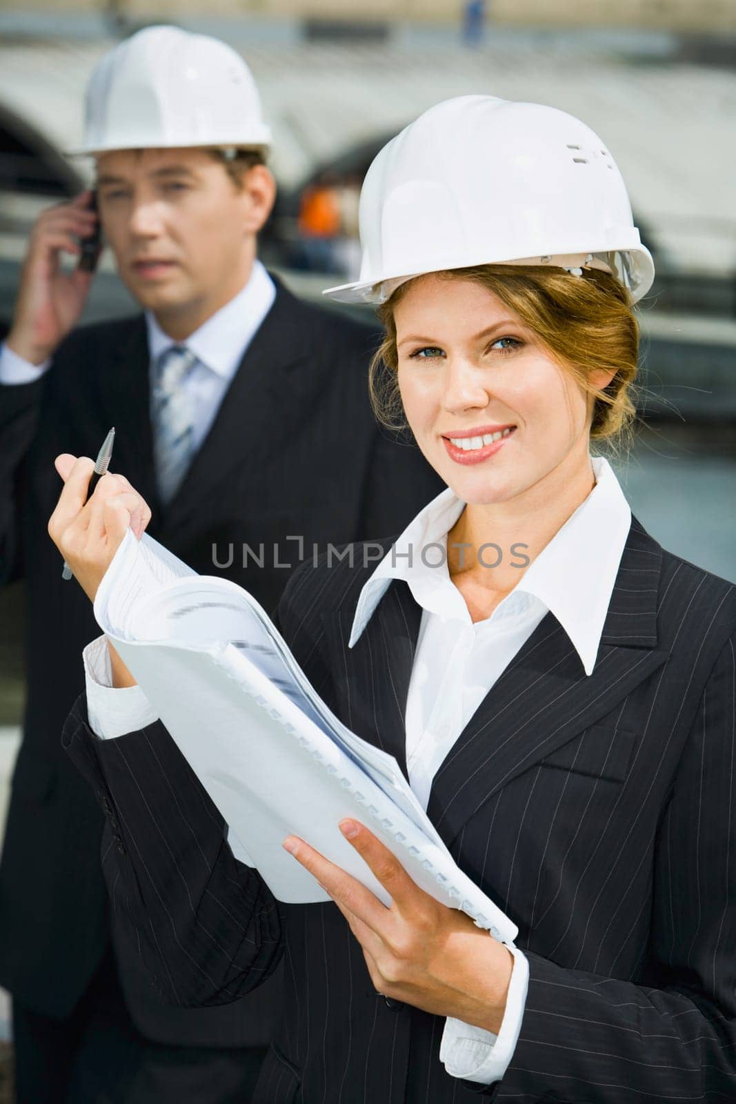 Businesswomen is holding architectural plan and pen on the background of her co-worker