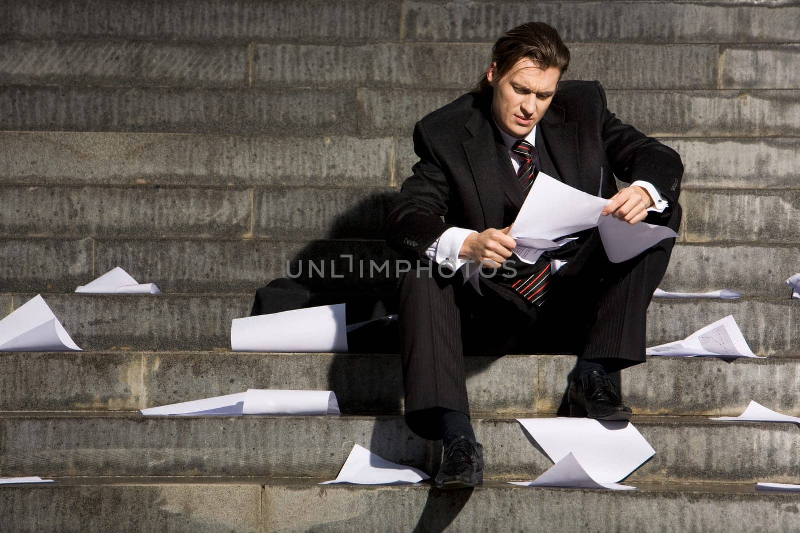 Portrait of depressed employee sitting in frustration on stairs with papers in hands