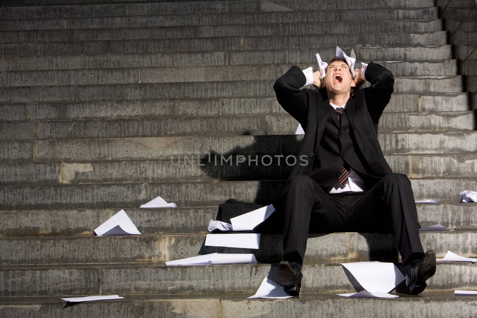 Despaired businessman screaming with papers in hands while sitting on staircase
