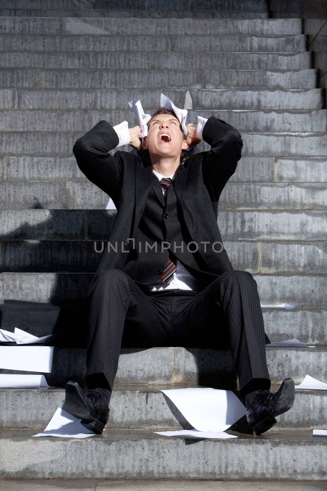 Despaired businessman screaming with papers in hands while sitting on staircase