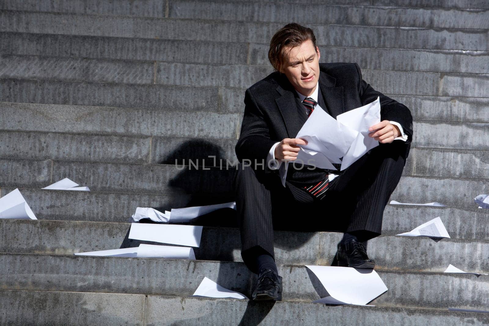 Portrait of depressed employee sitting in frustration on stairs with papers in hands