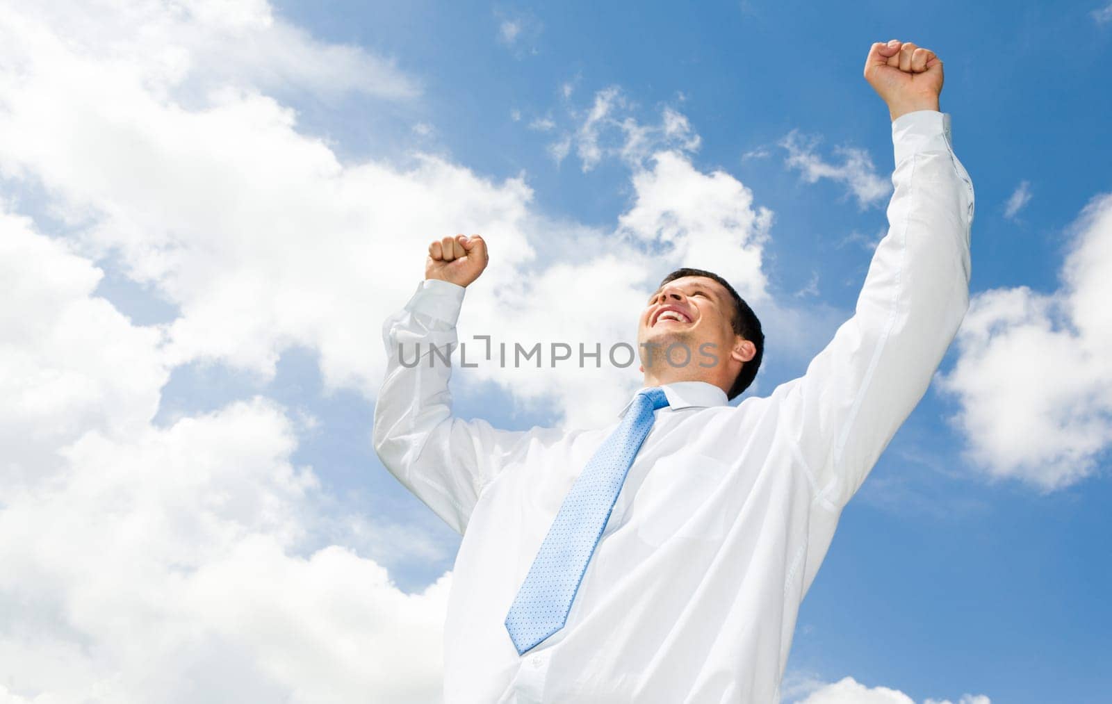 Portrait of happy businessman raising his hands with cloudy sky above him