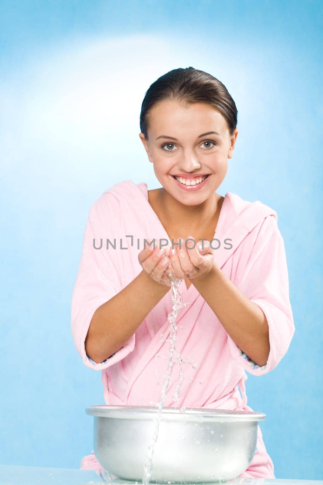 Portrait of happy female in pink bathrobe splashing water from wash-basin