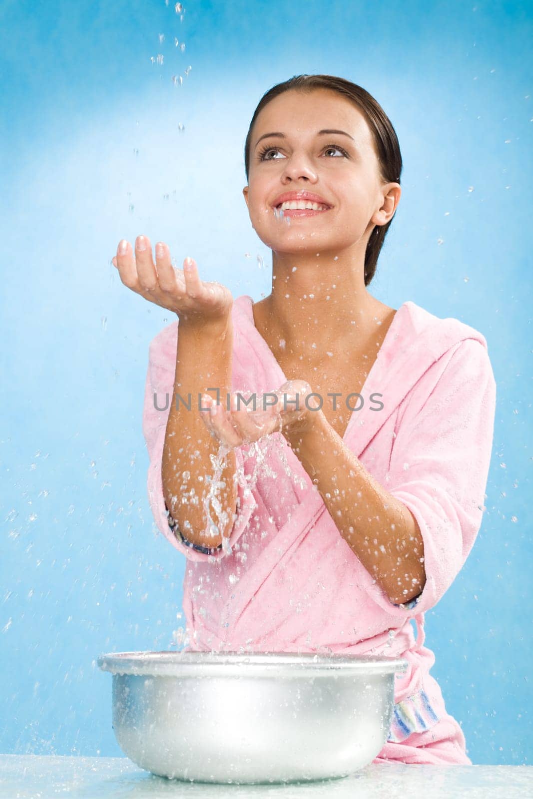 Portrait of happy female in pink bathrobe splashing water over blue background
