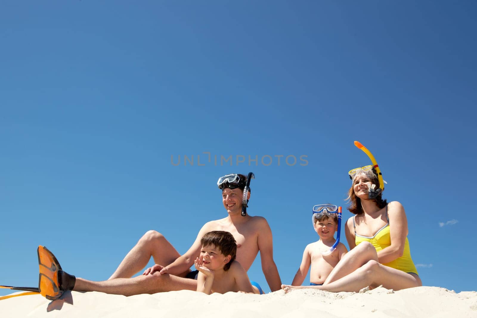 Portrait of modern family sitting on sandy beach against blue sky