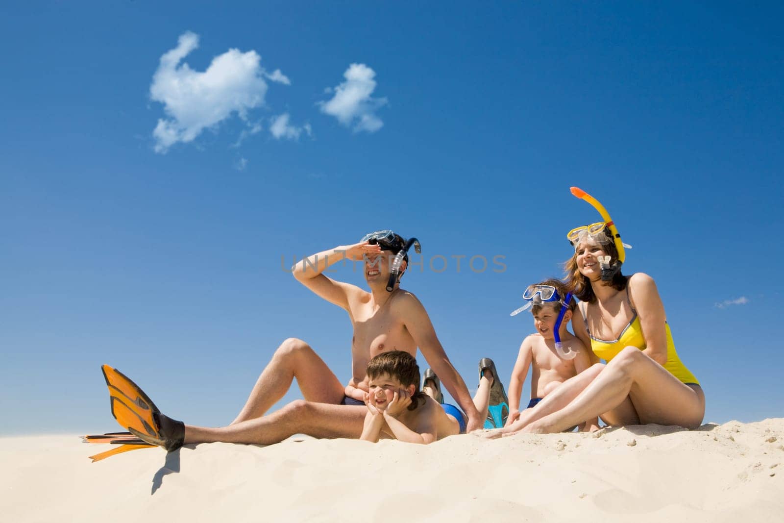 Portrait of modern family sitting on sandy beach against blue sky