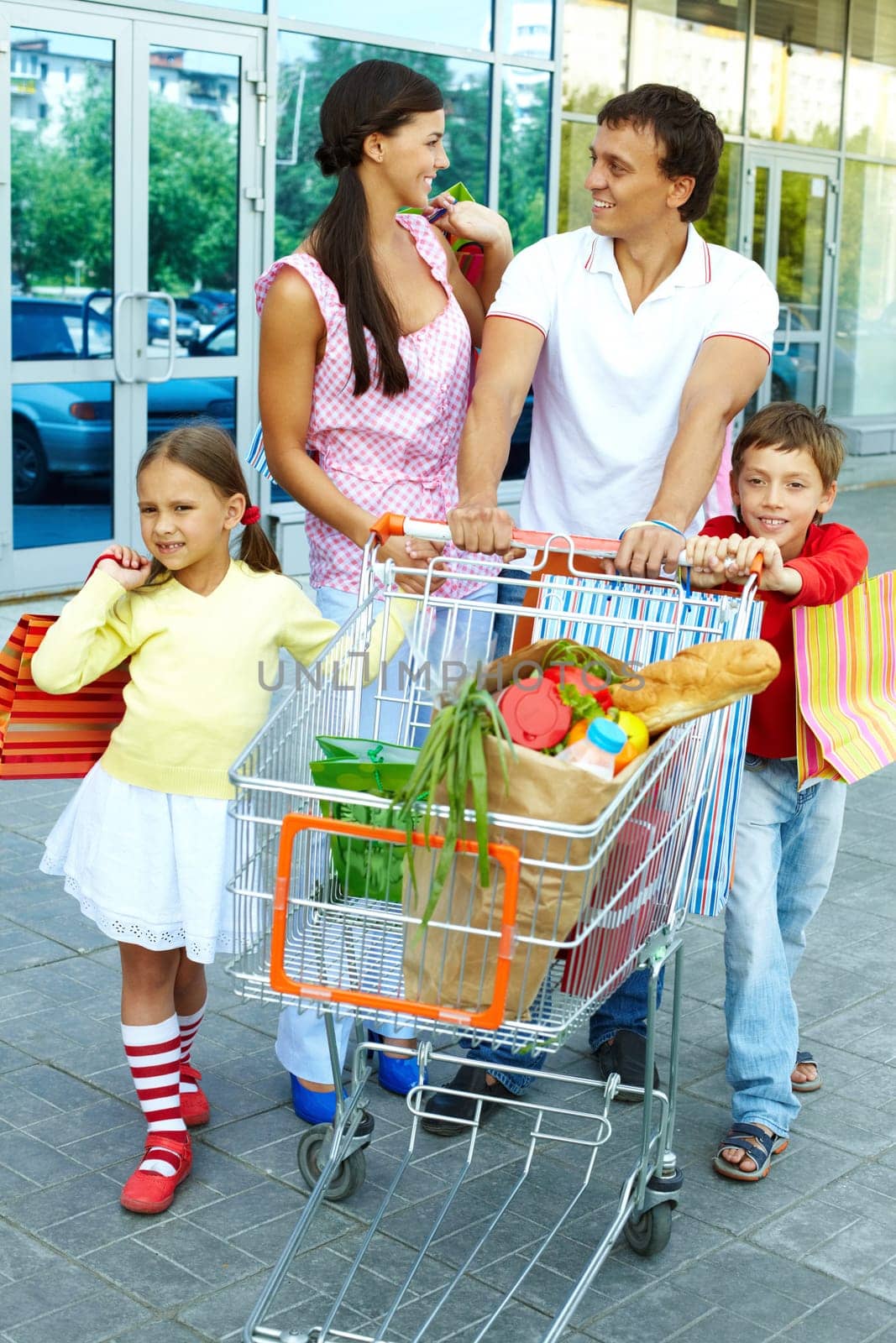 Couple with shopping bags and their two children pushing cart