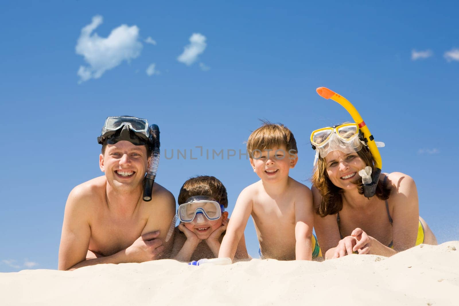 Portrait of diving family lying on sand against blue sky and smiling at camera