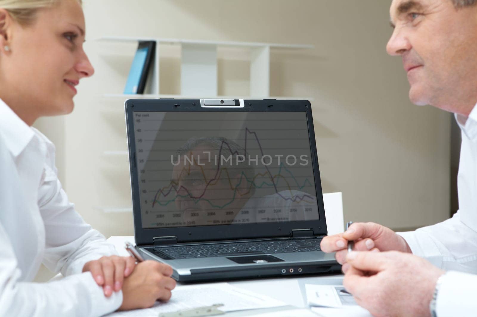 Portrait of successful business partners looking at each other with laptop on background
