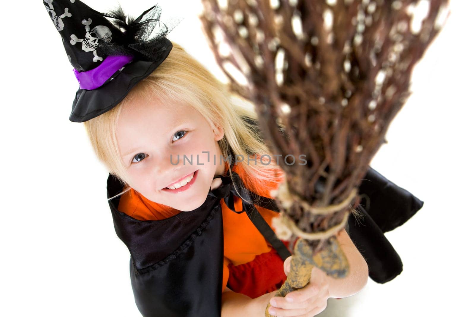 Above angle of girl in halloween costume and broom smilling at camera