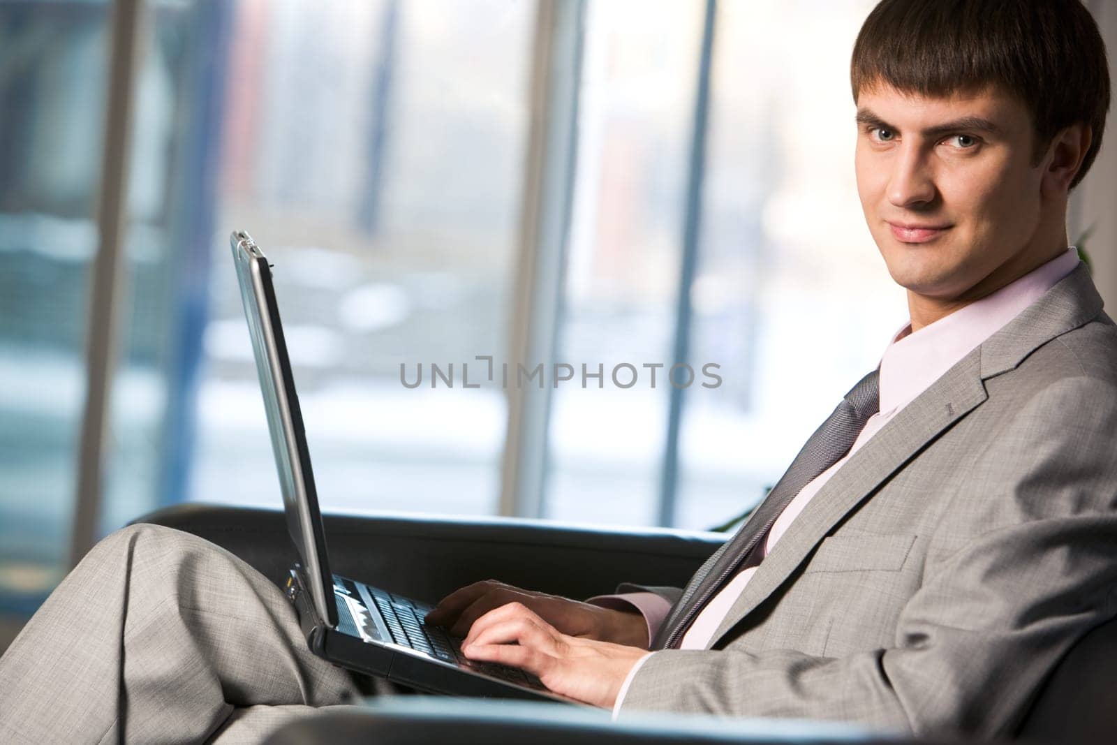 Handsome male typing on keyboard of laptop and looking at camera
