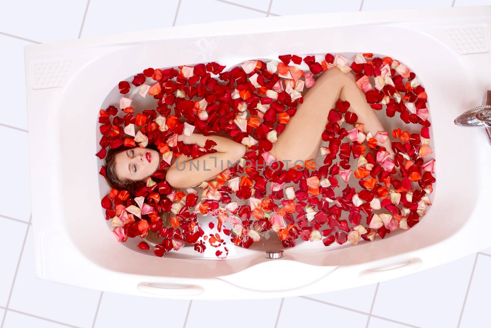 Pretty woman enjoys in the bathtub with petals of rose