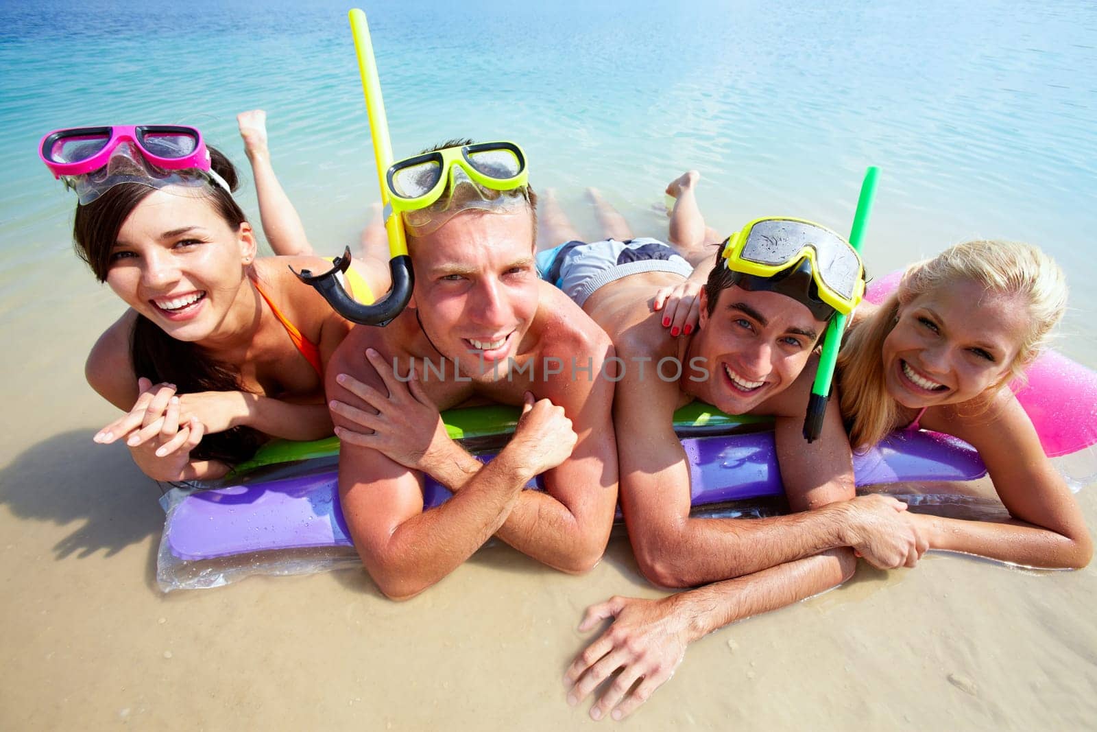 Four friends in scubas lying on sand by water