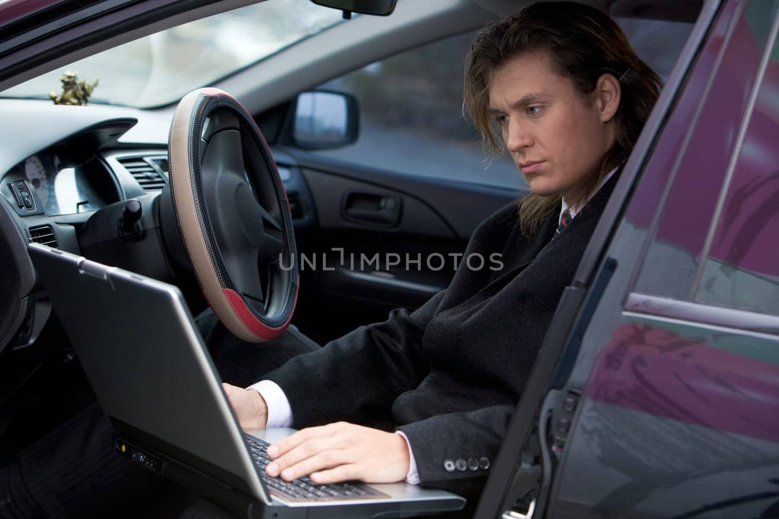 Portrait of serious businessman typing on laptop in the car