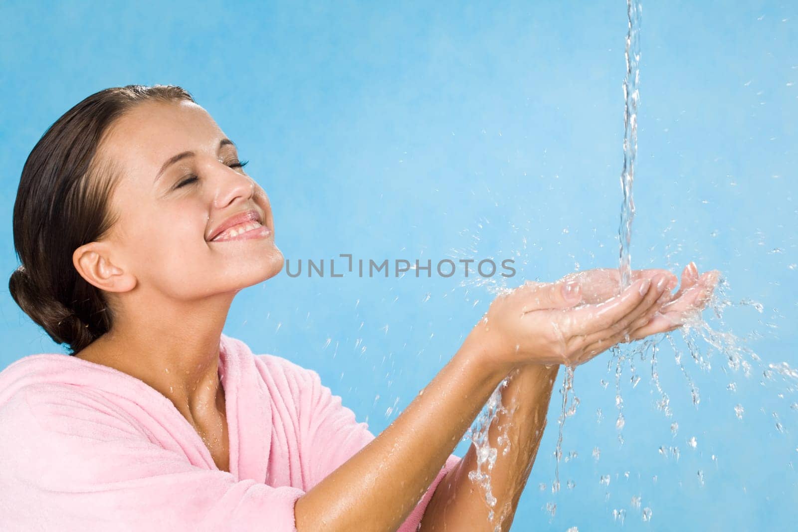 Joyful girl splashing pure water and enjoying it with her eyes closed over blue background