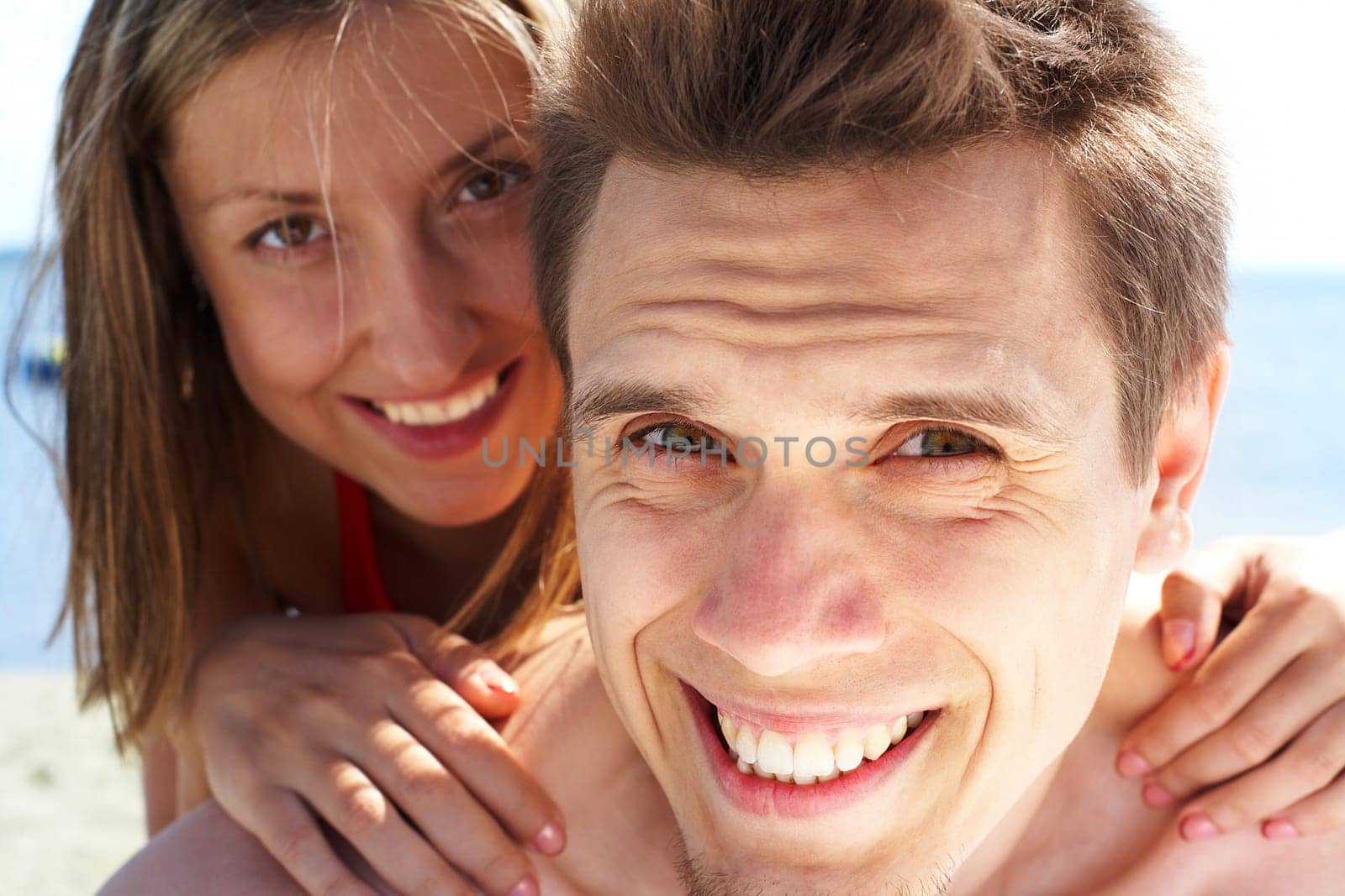 Photo of smiling guy looking at camera while pretty woman behind embracing him
