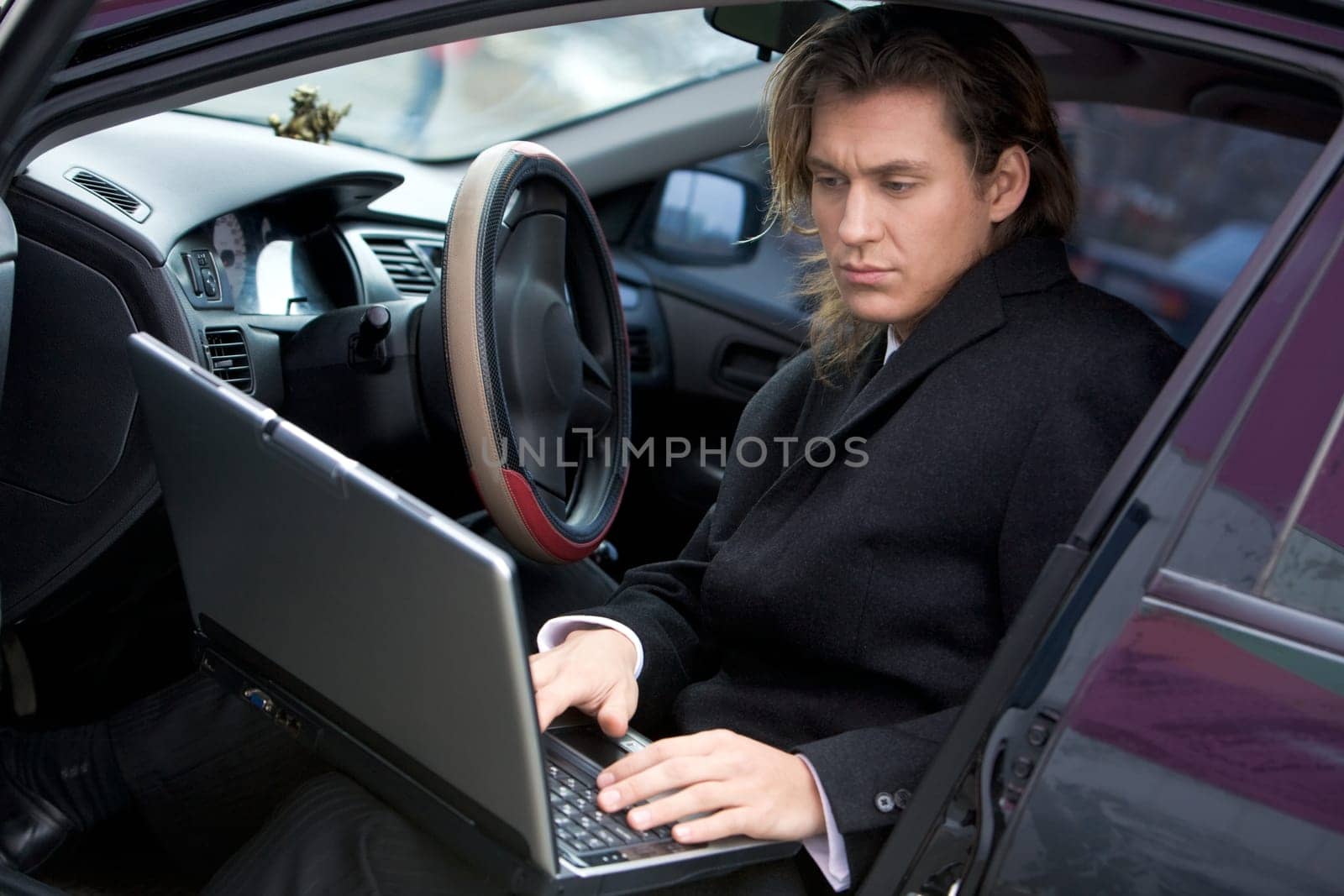 Portrait of handsome man typing on laptop while sitting in car