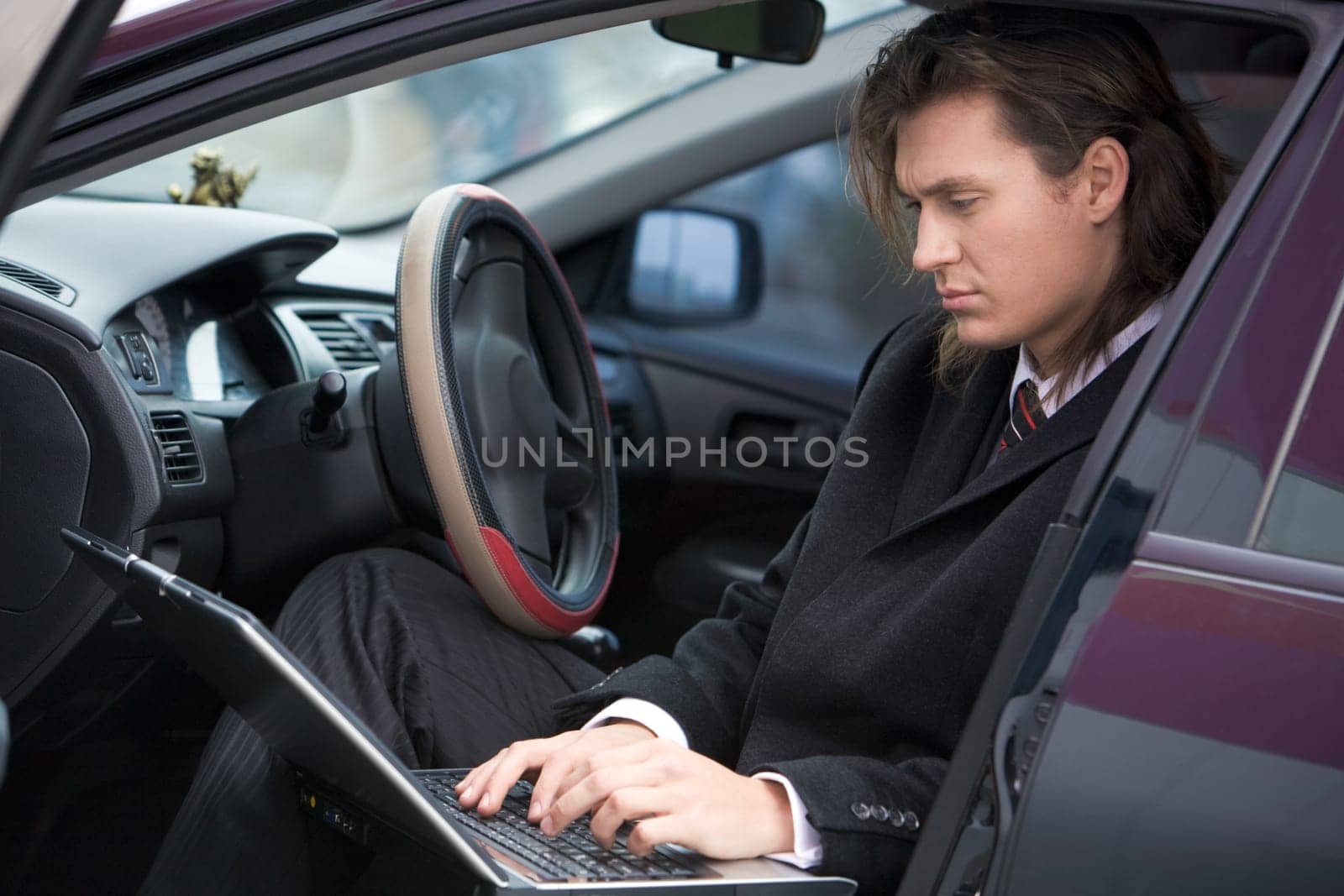 Photo of busy leader typing on his laptop with serious expression in car