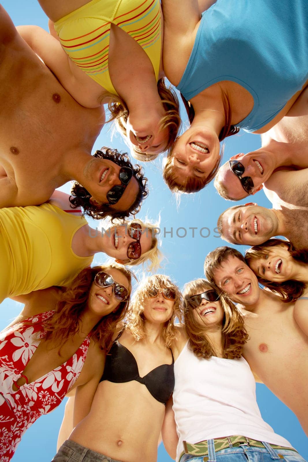 Below view of circle of friends looking at camera with blue sky above them