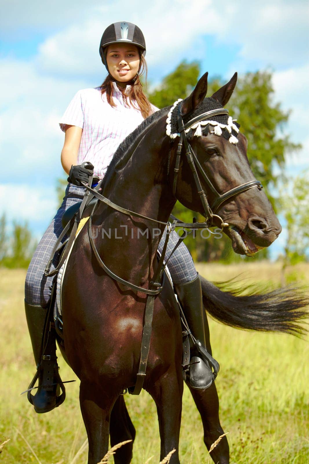 Image of happy female sitting on purebred horse and looking at camera outdoors