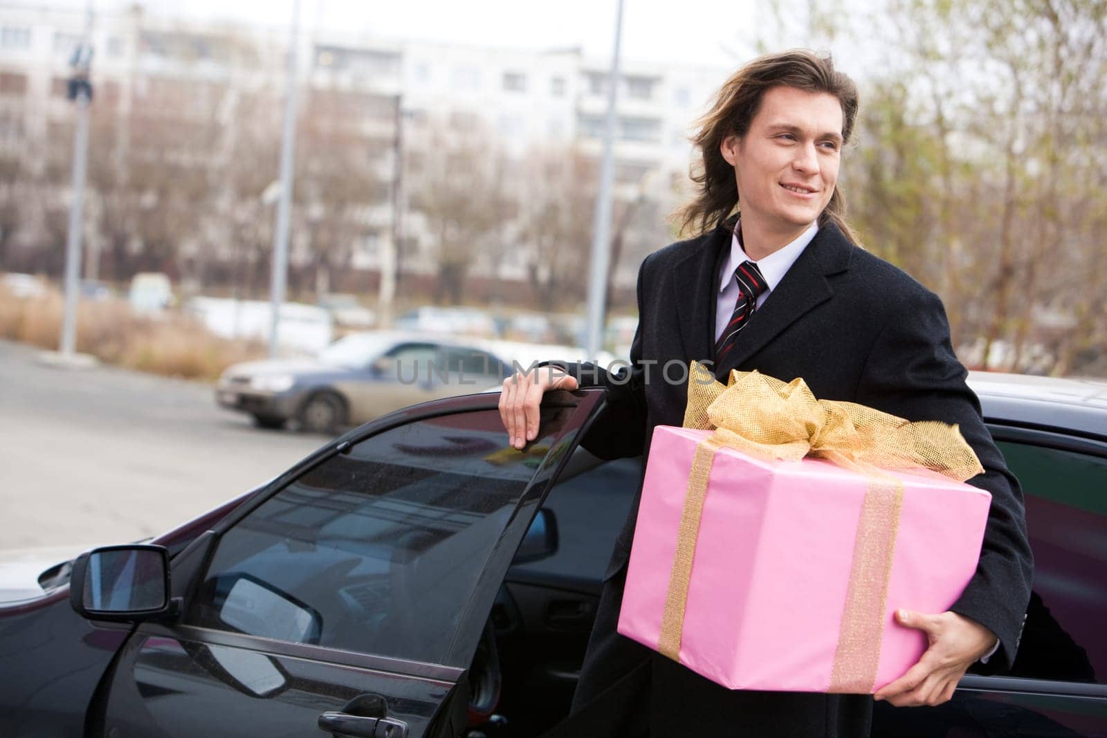 Portrait of happy businessman walking out of his car with big giftbox in hand