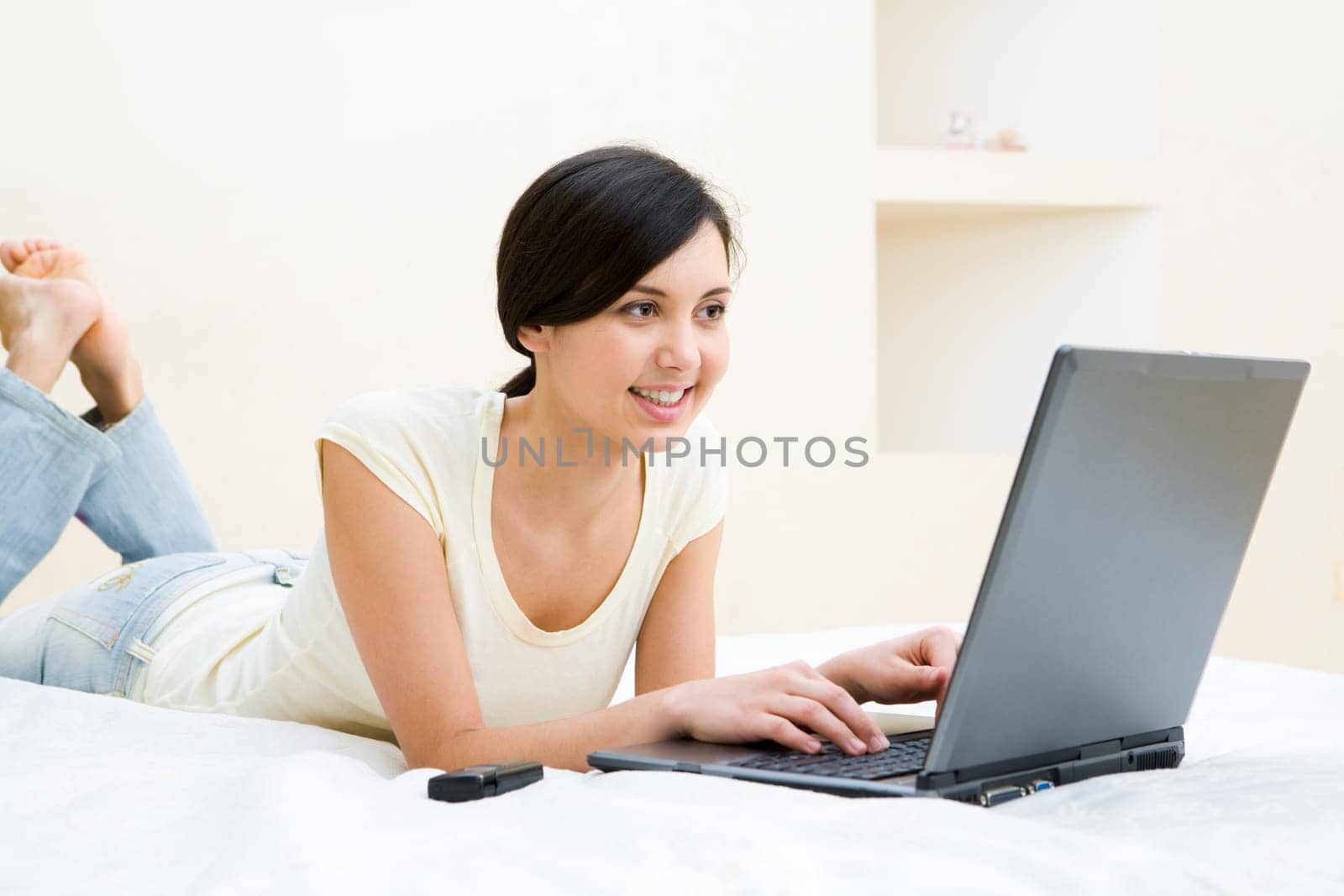 Image of pretty girl looking at laptop monitor while lying on bed in her room